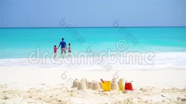白沙堡在白色海滩与塑料儿童玩具和家庭在海洋背景